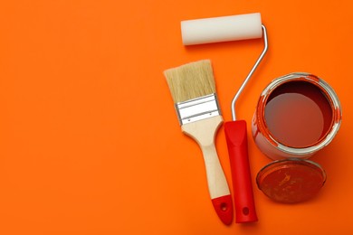 Can of orange paint, brush and roller on color background, flat lay. Space for text