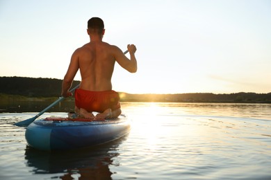 Photo of Man paddle boarding on SUP board in river at sunset, back view