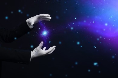 Image of Magician in gloves showing trick on dark background, closeup. Space for text
