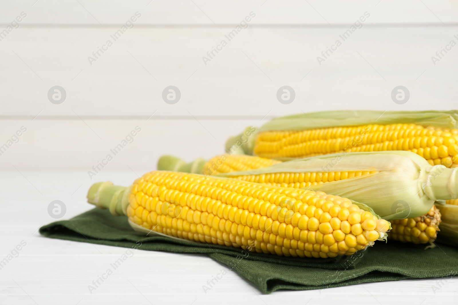 Photo of Tasty fresh corn cobs on white wooden table, space for text