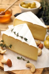 Photo of Tasty Camembert cheese with thyme, honey and nuts on wooden table
