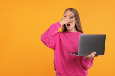 Photo of Embarrassed woman with laptop covering face on orange background, space for text
