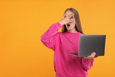 Embarrassed woman with laptop covering face on orange background, space for text