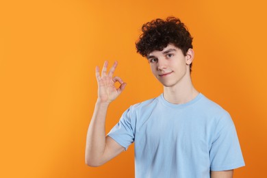 Portrait of teenage boy showing ok gesture on orange background. Space for text