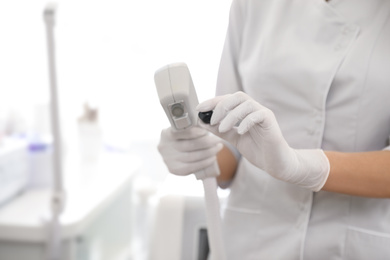 Young woman holding professional laser epilator in beauty salon, closeup