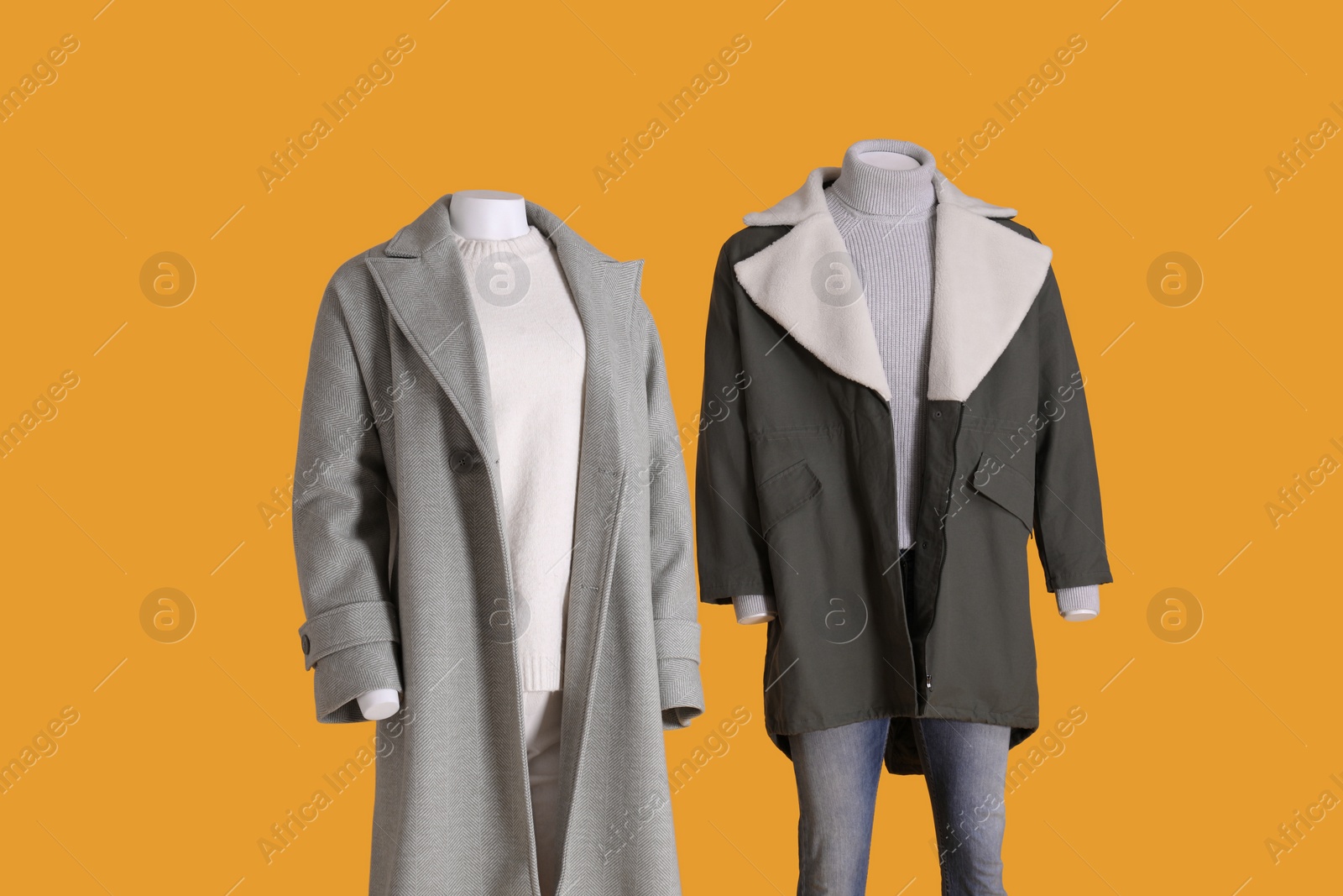 Photo of Mannequins dressed in stylish coat, jacket, sweater and turtleneck on orange background