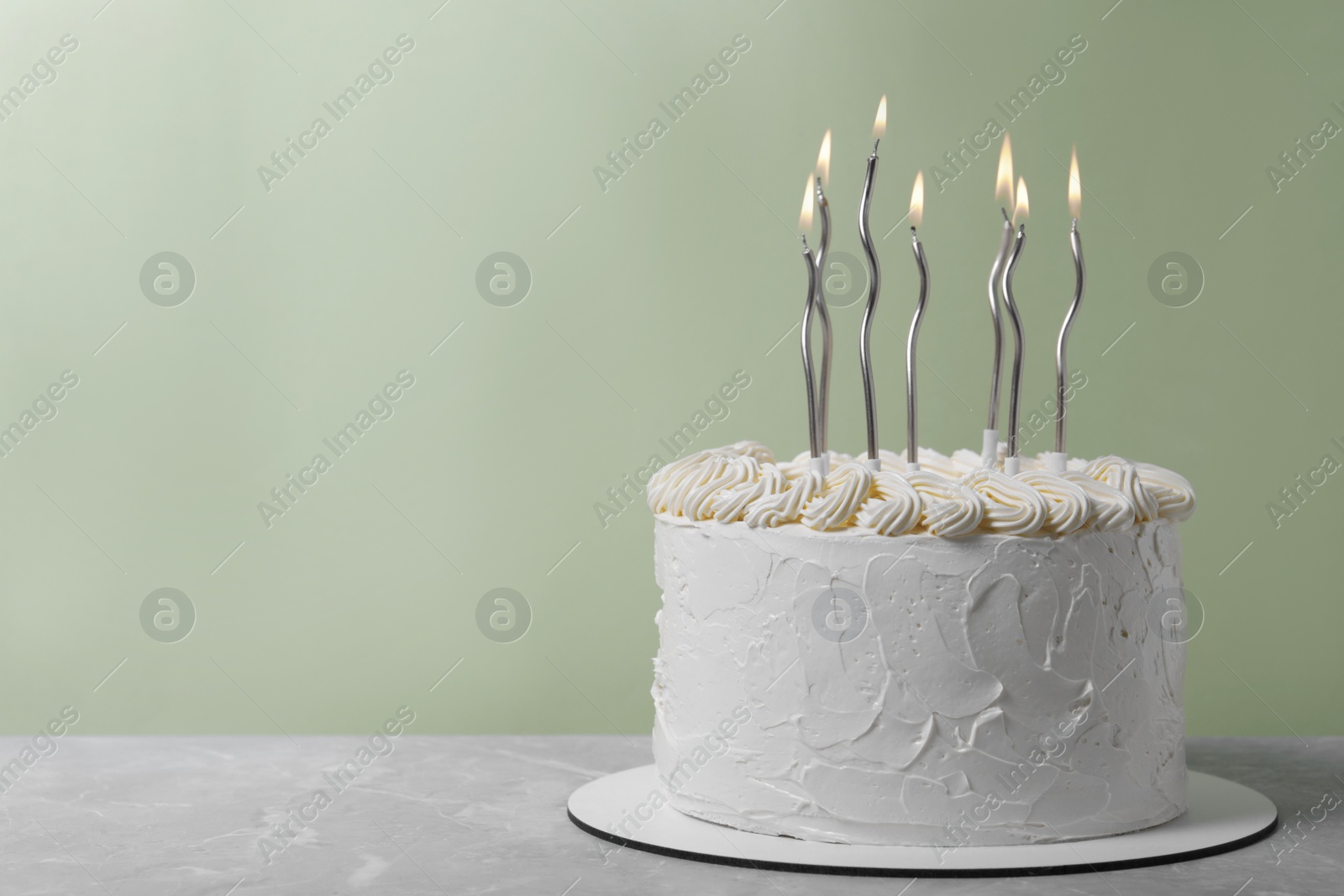 Photo of Delicious cake with cream and burning candles on grey table. Space for text