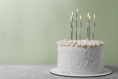 Photo of Delicious cake with cream and burning candles on grey table. Space for text