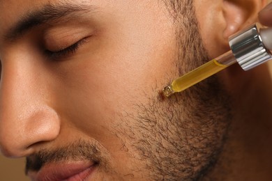 Photo of Handsome man applying cosmetic serum onto face, closeup