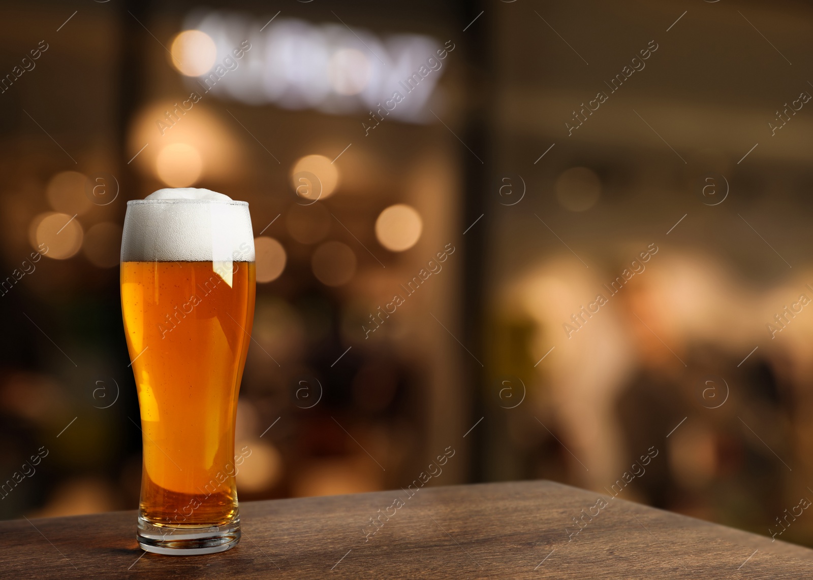 Image of Glass with cold tasty beer on wooden table in pub, space for text