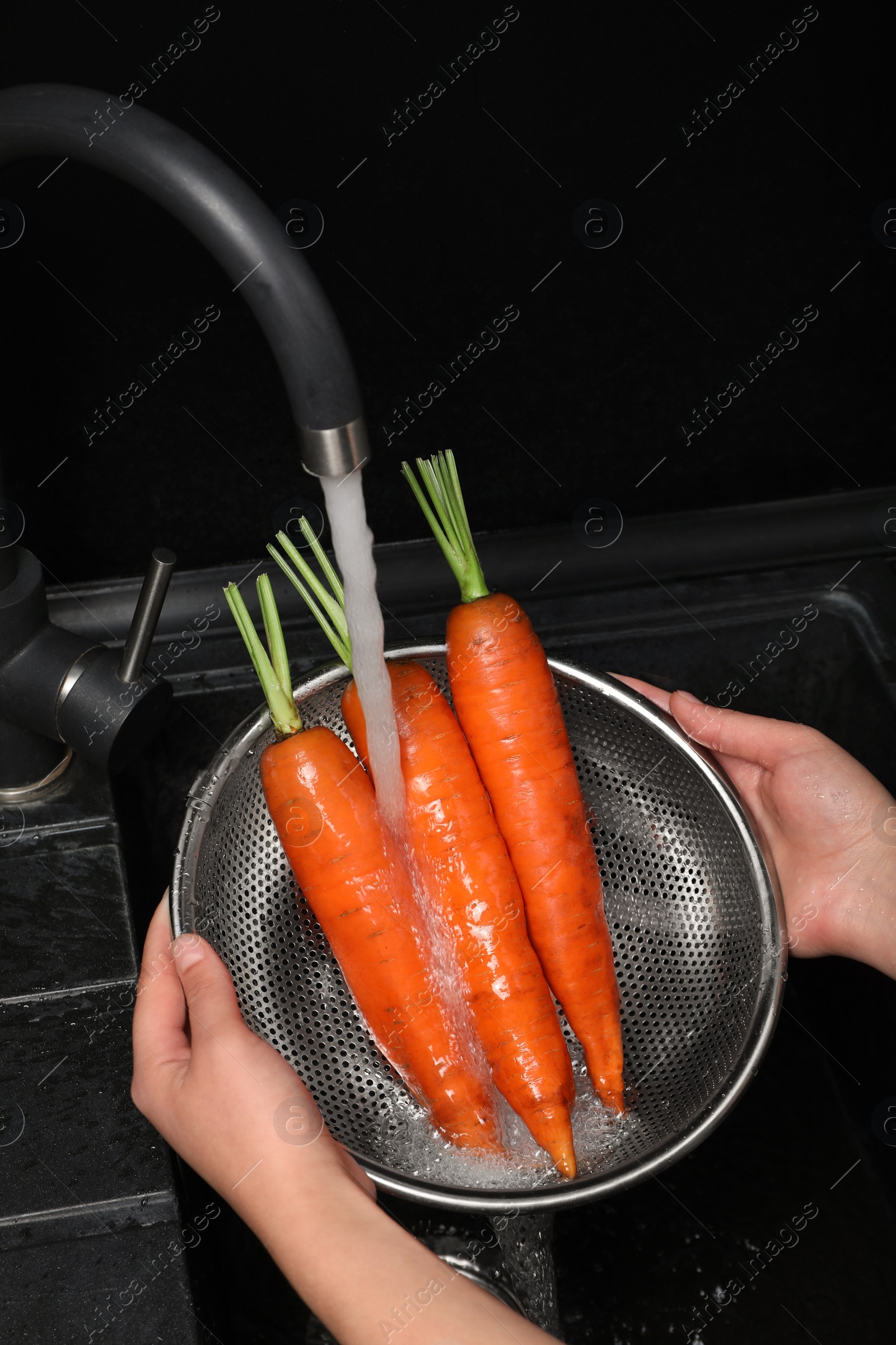 Photo of Woman washing fresh ripe juicy carrots under tap water in sink, above view