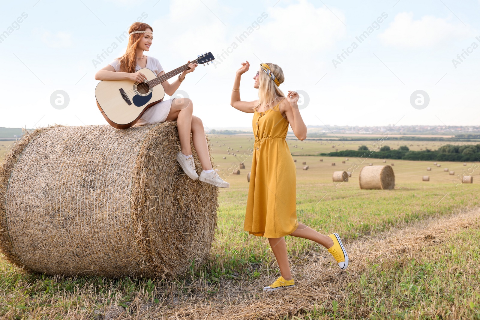 Photo of Beautiful hippie woman dancing while her friend playing guitar in field, space for text