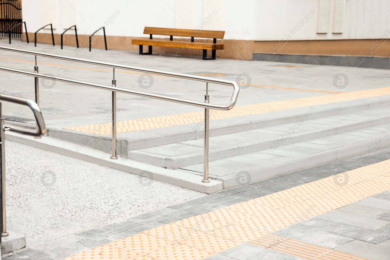 Photo of Outdoor stairs with ramp, metal railing and tactile tiles. Public environment accessibility