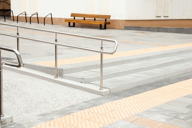 Photo of Outdoor stairs with ramp, metal railing and tactile tiles. Public environment accessibility