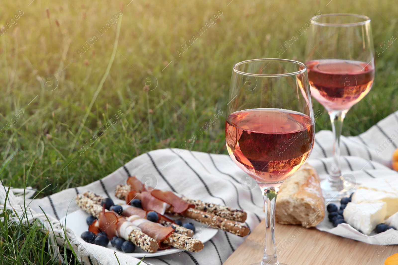 Photo of Glasses of delicious rose wine and food on picnic blanket outdoors