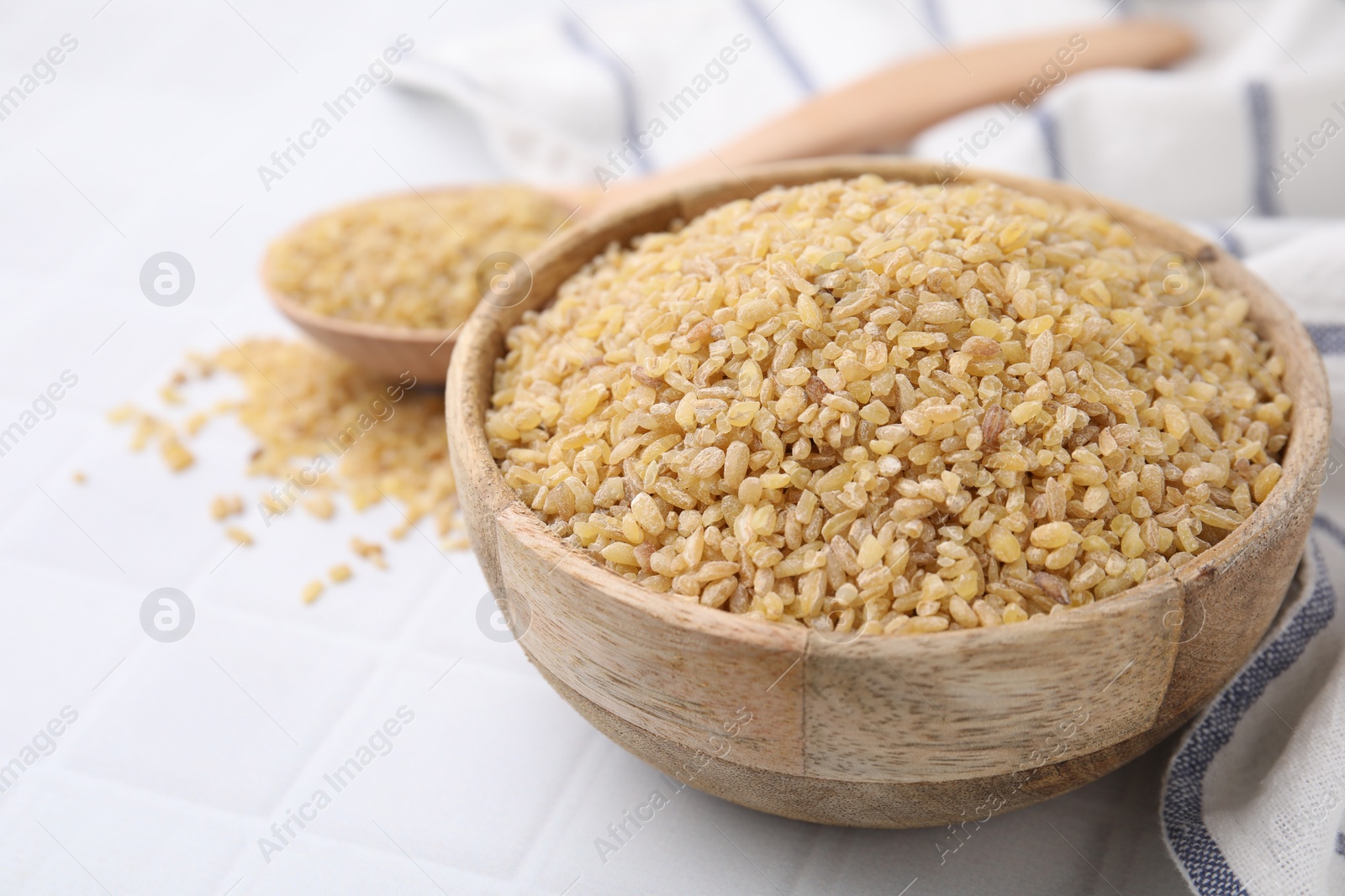 Photo of Raw bulgur in bowl on white table, closeup