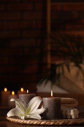 Spa composition with burning candles, lily flower and towels on wooden table in wellness center, space for text