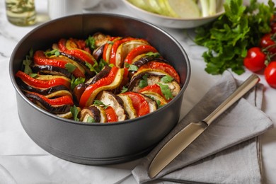 Delicious ratatouille in round baking pan and knife on table