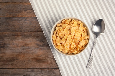 Photo of Bowl with healthy cornflakes for breakfast on wooden table, top view. Space for text