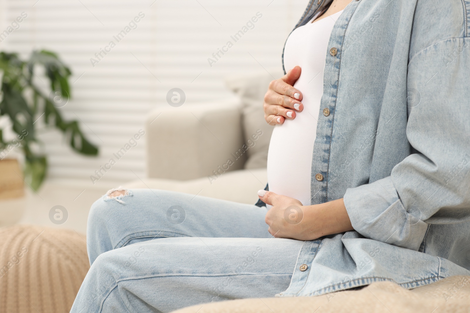 Photo of Pregnant woman touching her belly on sofa at home, closeup