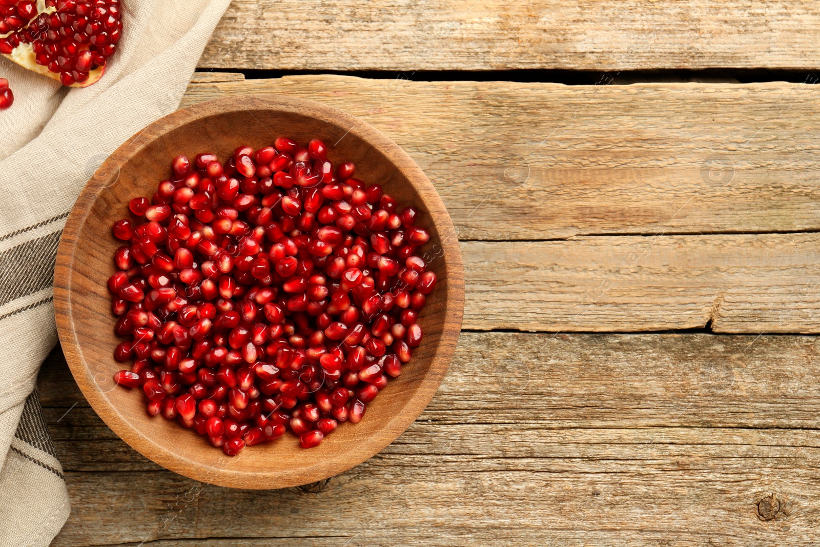 Photo of Ripe juicy pomegranate grains in bowl on wooden table, top view. Space for text