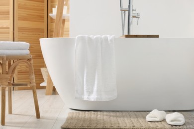 Photo of Stylish tub, wicker stool, slippers and soft towels in bathroom