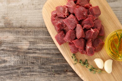 Photo of Pieces of raw beef meat, oil and garlic on wooden table, top view. Space for text