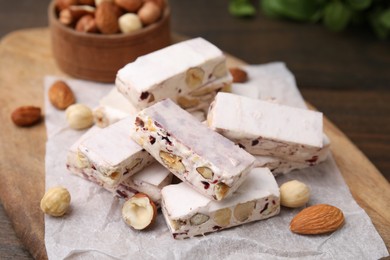 Photo of Pieces of delicious nutty nougat on wooden board, closeup