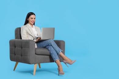 Photo of Happy woman with laptop sitting in armchair on light blue background, space for text