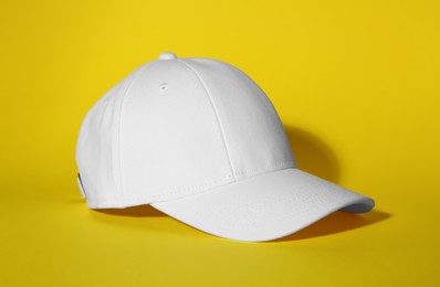 Photo of Stylish white baseball cap on yellow background