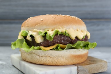 Photo of Delicious cheeseburger with lettuce, sauce and patty on table, closeup
