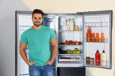 Happy young man near open refrigerator indoors