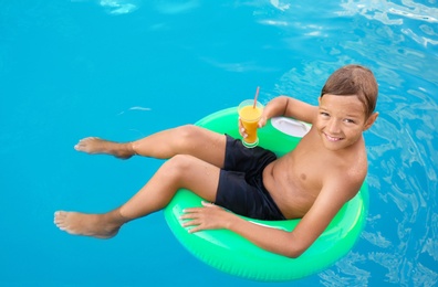 Happy cute boy on inflatable ring with drink in swimming pool