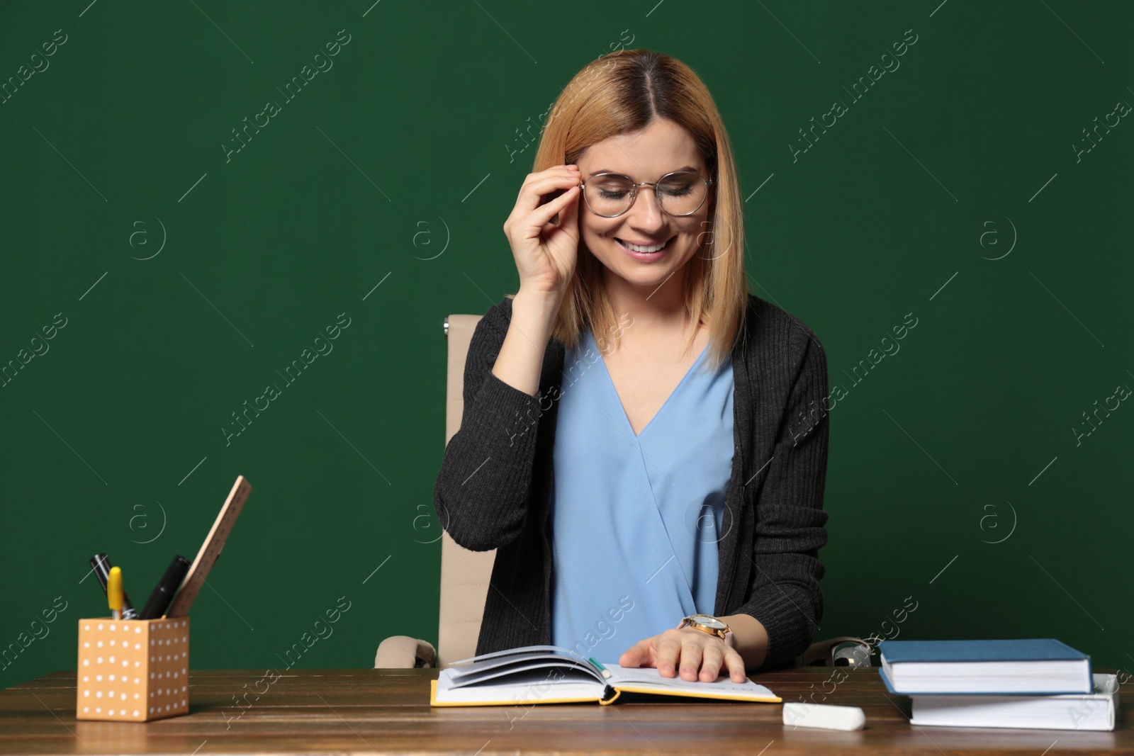 Photo of Portrait of beautiful teacher sitting at table near chalkboard