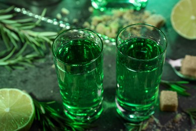 Photo of Absinthe in shot glasses, lime and rosemary on table, closeup. Alcoholic drink