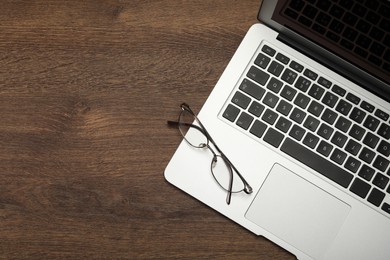 Photo of Modern laptop and glasses on wooden table, top view. Space for text