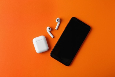 Photo of Wireless earphones, mobile phone and charging case on orange background, flat lay. Space for text