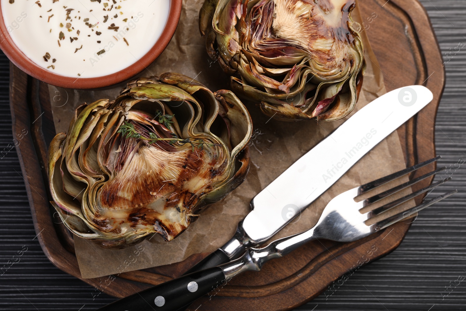 Photo of Tasty grilled artichoke and sauce on dark wooden table, top view