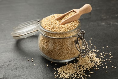Photo of Dry quinoa seeds and scoop in glass jar on black table, closeup