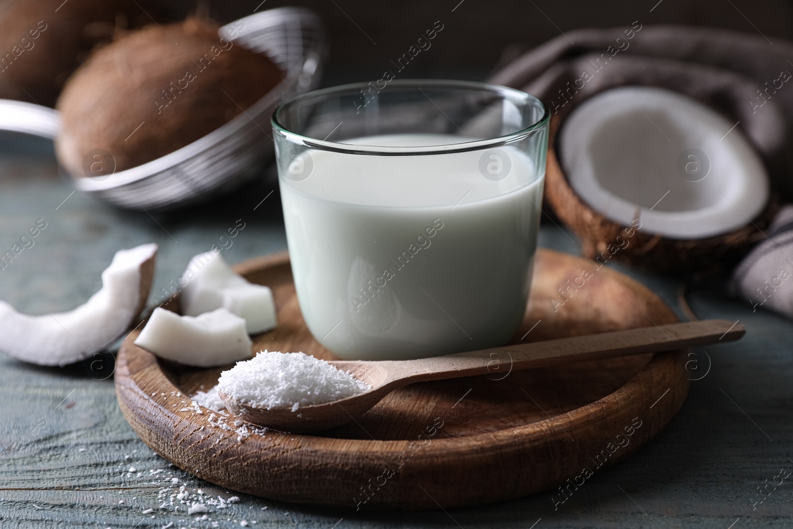 Photo of Glass of delicious coconut milk, spoon with flakes and nuts on wooden table, closeup