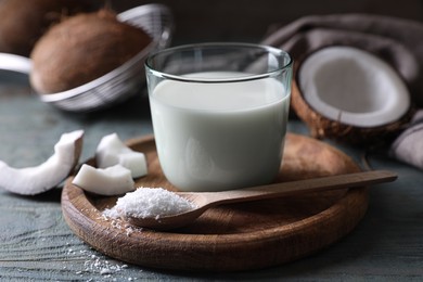 Photo of Glass of delicious coconut milk, spoon with flakes and nuts on wooden table, closeup