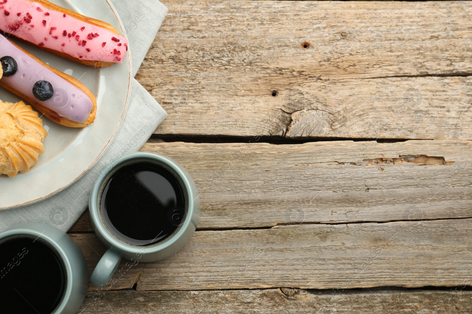 Photo of Aromatic coffee in cups, tasty eclairs and profiterole on wooden table, top view. Space for text