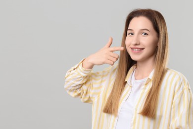 Photo of Portrait of smiling woman pointing at her dental braces on grey background. Space for text