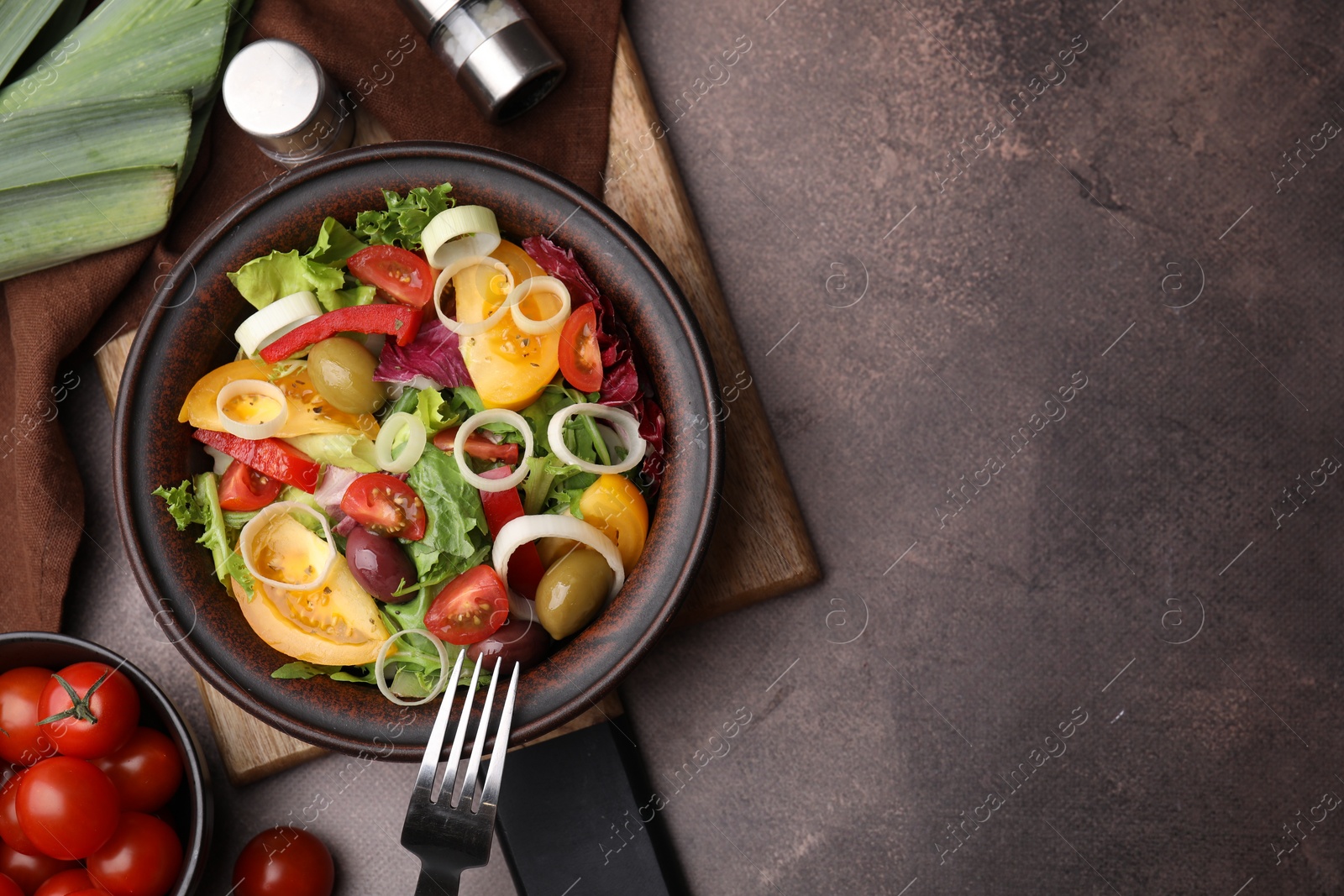 Photo of Bowl of tasty salad with leek and olives served on brown table, flat lay. Space for text