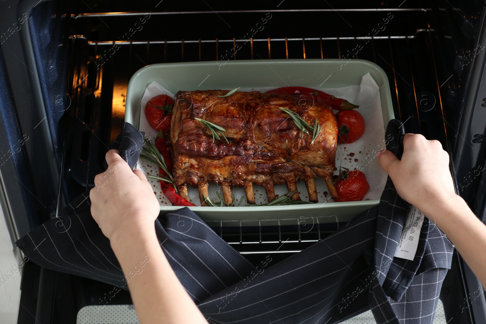 Photo of Woman taking delicious ribs out of oven, closeup