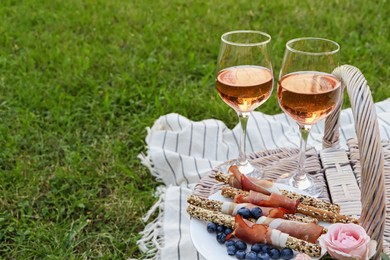 Glasses of delicious rose wine, food and basket on picnic blanket outdoors