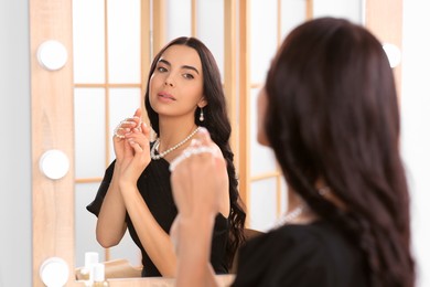 Young woman wearing elegant pearl jewelry near mirror indoors