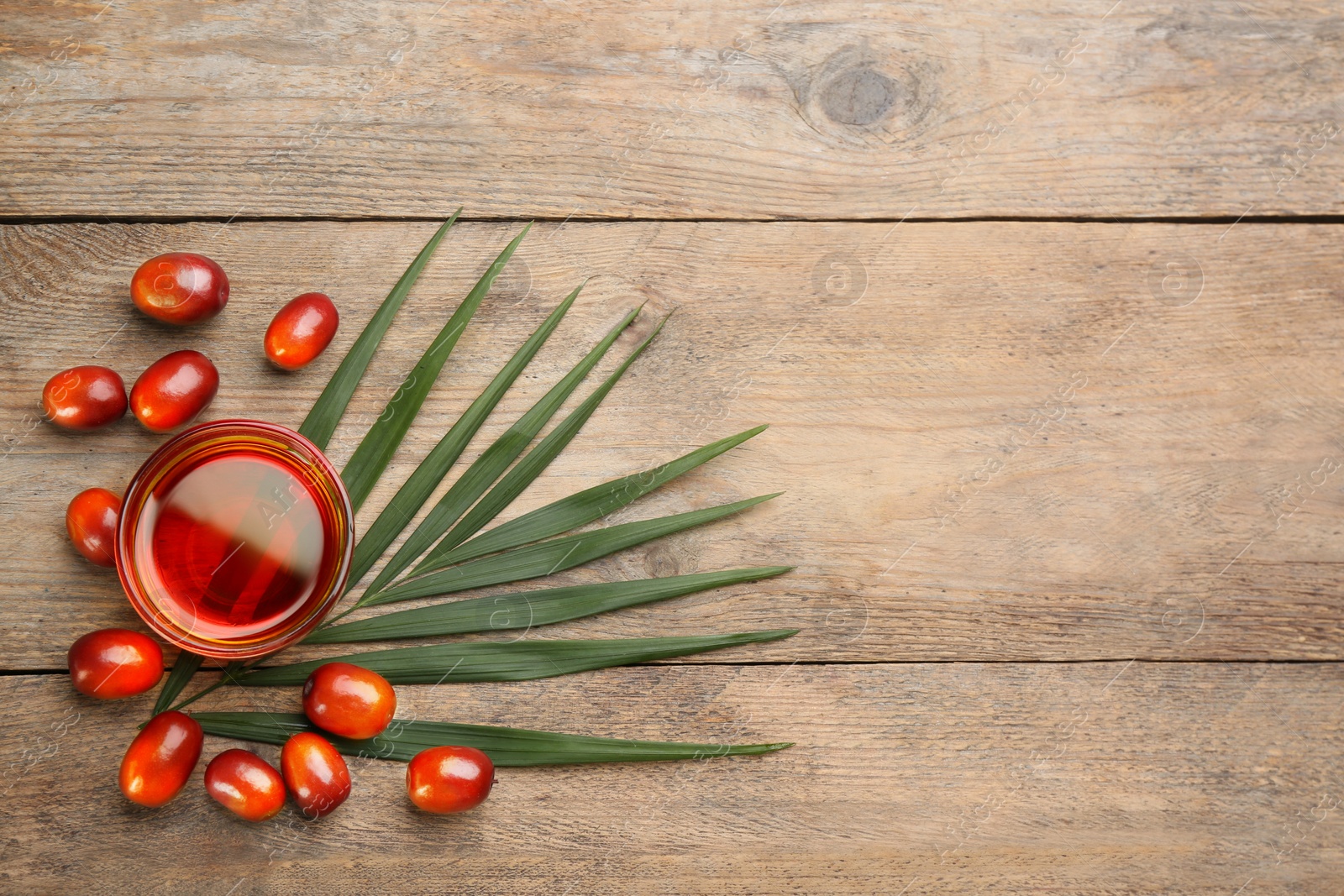 Photo of Palm oil in glass, tropical leaf and fruits on wooden table, flat lay. Space for text