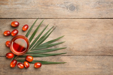 Palm oil in glass, tropical leaf and fruits on wooden table, flat lay. Space for text