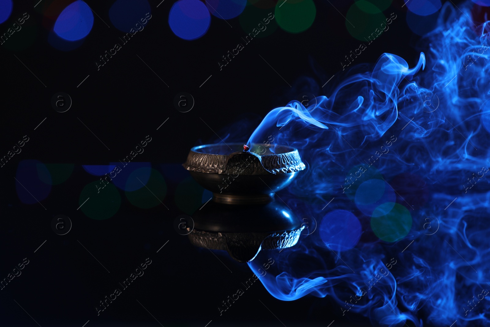 Photo of Blown out diya on dark background with blurred lights, space for text. Diwali lamp